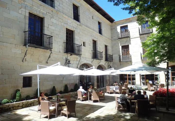 Disfruta de un día soleado donde comer en Santillana del Mar, con mesas al aire libre bajo sombrillas blancas, rodeado de arquitectura de piedra.