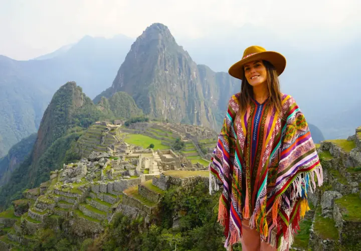 Mujer con poncho colorido y sombrero en Machu Picchu, una experiencia inolvidable al viajar a Perú.