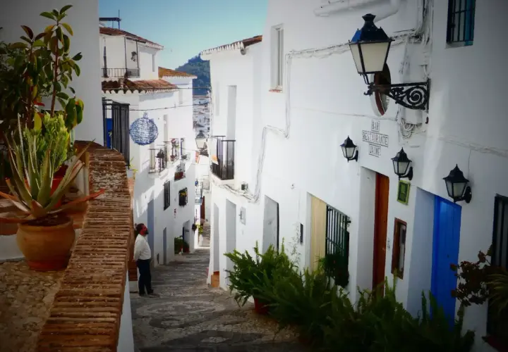 Hombre mira callejuela blanca en Frigiliana. Aquí puedes encontrar dónde comer en Frigiliana, con un bar y restaurante.