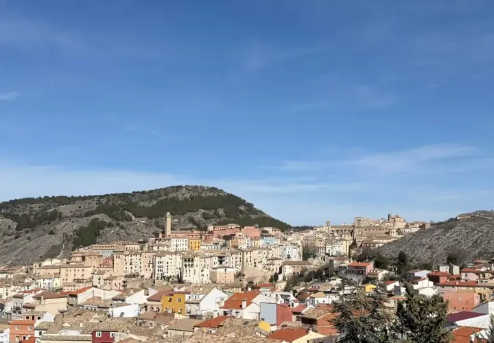 Vista panorámica de Cuenca, con sus casas de colores y tejados anaranjados, asentadas en una ladera rocosa bajo un cielo azul. Ideal para saber qué ver en Cuenca en un día.