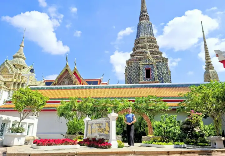 Disfrutando de un free tour en Bangkok, una mujer posa frente a templos tailandeses y pagodas ornamentadas bajo un cielo azul.