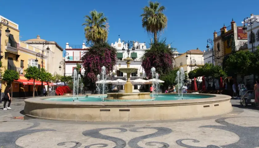Fuente en plaza con palmeras y edificios blancos, ideal para saber qué ver en Sanlúcar de Barrameda.
