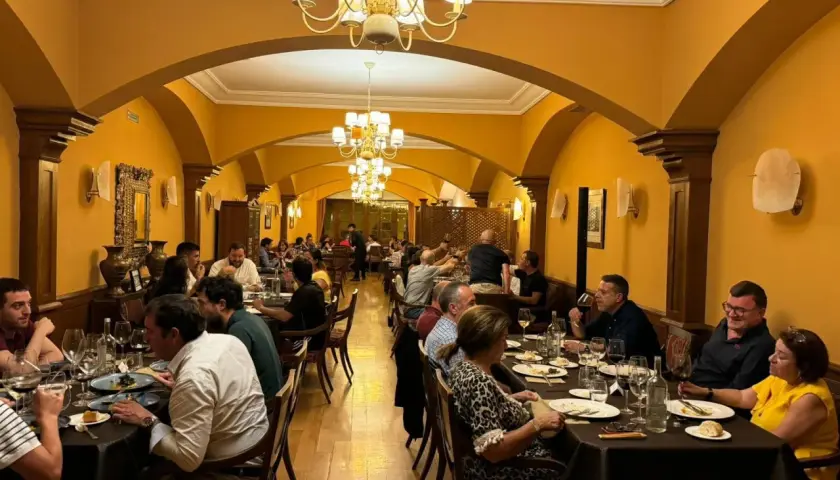 Gente disfrutando de una cena en un elegante salón con arcos y lámparas doradas. Un ambiente perfecto para comer en Olite.
