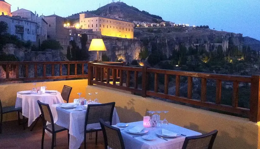 Mesas puestas en terraza con vistas a la ciudad iluminada. Un lugar ideal donde comer en Cuenca al anochecer.
