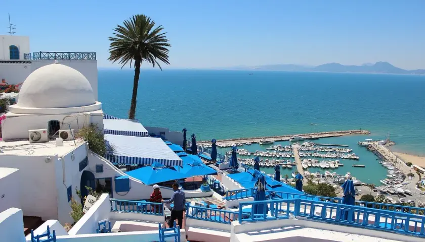 Vista de un puerto deportivo y el mar azul desde un café con cúpulas blancas y sombrillas azules. ¡Un sueño para viajar a Túnez!