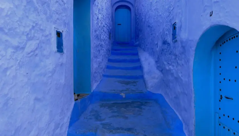 Callejón azul en Chefchaouen, con escalones que suben hacia una puerta. A pesar de su belleza, Chefchaouen es peligroso para los que se pierden en sus laberintos.