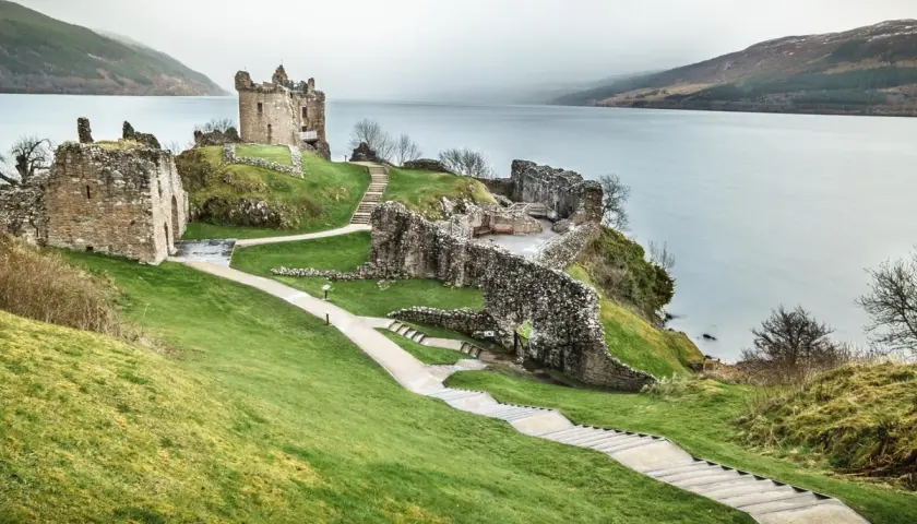 Ruinas de un castillo en una colina verde junto a un lago, ideal para un viaje a Escocia 7 días.