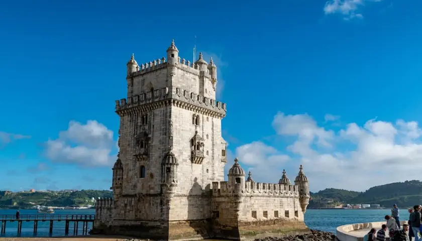 Torre de Belém, un sitio histórico perfecto para un free tour Lisboa. El cielo azul y el agua reflejan su belleza.