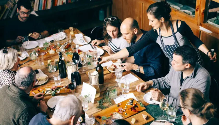 Gente disfrutando de una comida compartida en Barcelona. Una mesa llena de platos, botellas y copas.