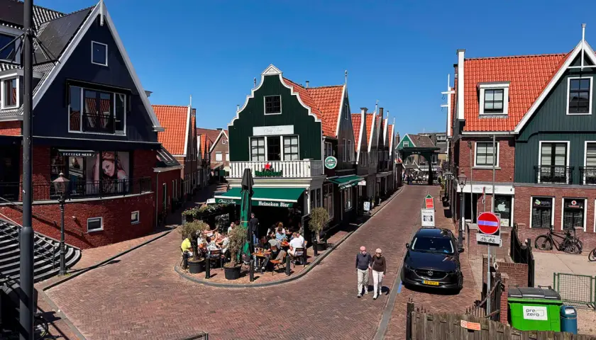Un paseo por un pueblo holandés con casas de tejados rojos y fachadas coloridas. Un lugar ideal que ver en Holanda, con gente disfrutando en una terraza.