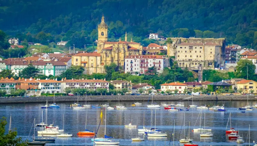 Vista de Hondarribia que ver: un puerto con veleros y barcos, y al fondo la iglesia y edificios históricos.