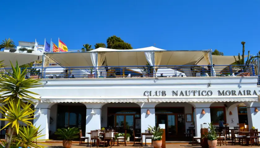 Club Náutico Moraira, ideal para comer en Moraira con vistas al mar. Banderas ondean bajo el sol.