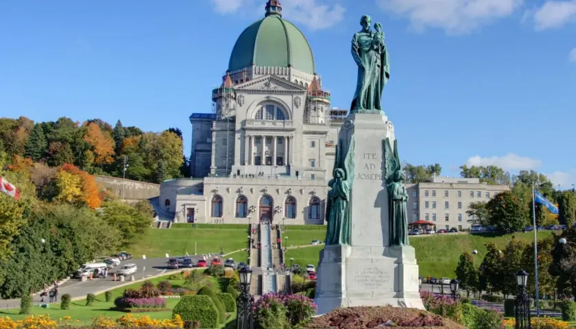 Estátua de São José frente a uma basílica imponente, ideal para visitas guiadas Montreal. Outono com árvores coloridas.
