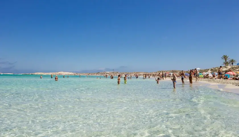 Gente disfrutando de las **mejores playas de Formentera**, con aguas cristalinas y arena blanca bajo un cielo azul.