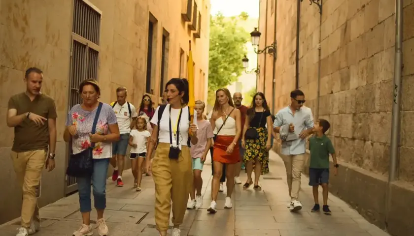 Un grupo disfruta de un free tour en Salamanca, guiado por una mujer con un micrófono, mientras pasean por una calle estrecha y empedrada.