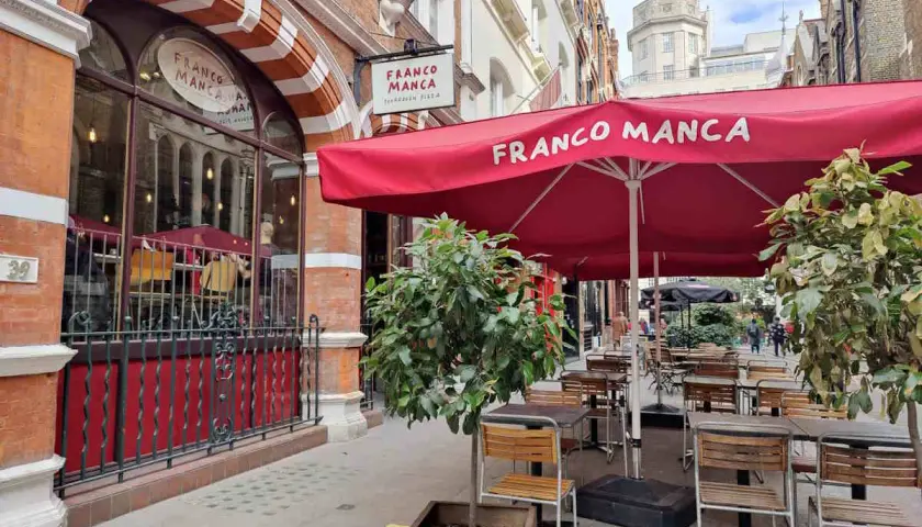 Franco Manca, un lugar ideal donde comer en Londres, con mesas al aire libre bajo sombrillas rojas.