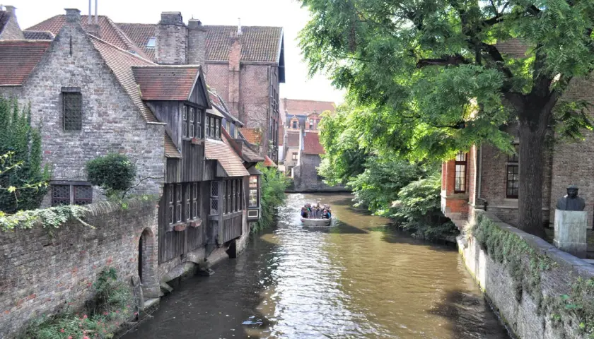 Un paseo en barco por los canales es ideal para ver Brujas en un día. Casas antiguas y árboles frondosos bordean el agua.