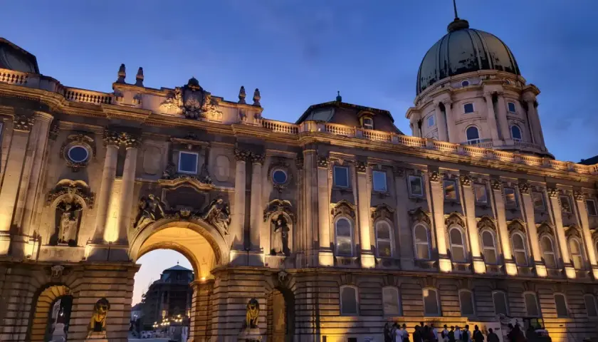 Palacio de Buda iluminado al atardecer, ideal para **free tours Budapest**. Una joya arquitectónica con cúpula verde y detalles ornamentados.