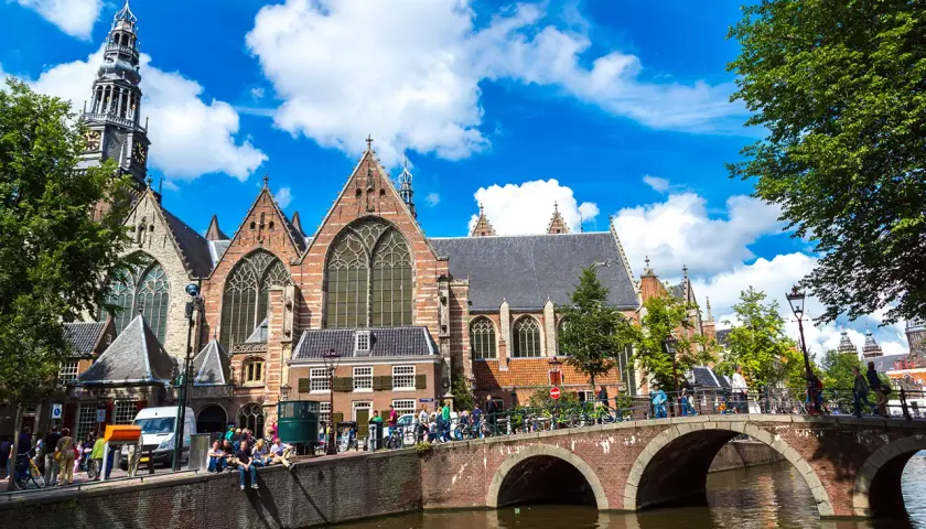 Gente disfrutando de un free tour en Ámsterdam, cruzando un puente sobre un canal frente a una iglesia histórica.