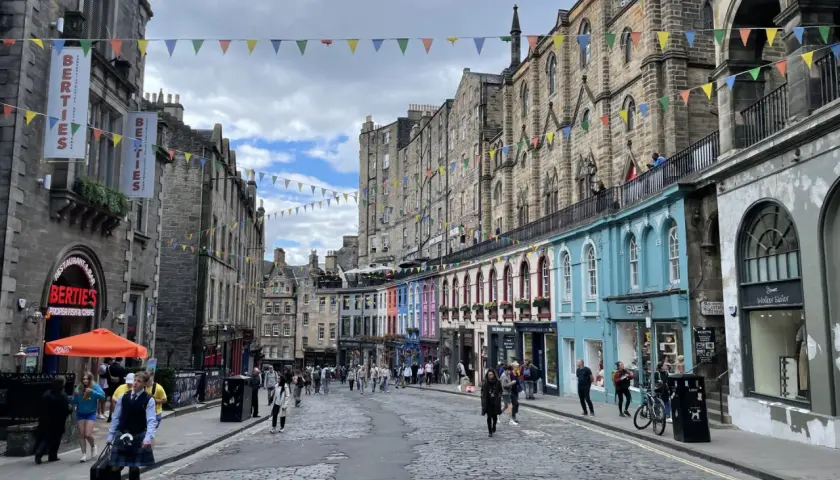 Calle adoquinada de Edimburgo, con edificios históricos y coloridas fachadas. Gente paseando, ideal para un **free tour Edimburgo**.