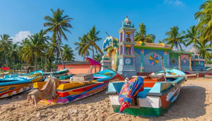 Barcas coloridas en la playa de Sri Lanka, con un templo vibrante al fondo. Es seguro viajar a Sri Lanka y disfrutar de su belleza.