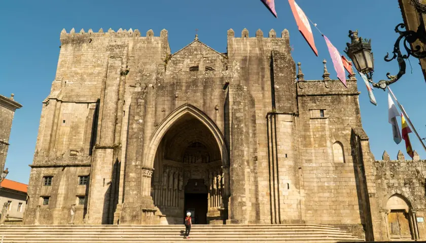 Impresionante Catedral de Tui, un lugar imprescindible que ver en Tui. Fachada de piedra con arco gótico y una persona en las escaleras.