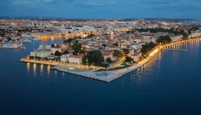 Vista aérea de Zadar al anochecer. La ciudad iluminada se extiende a lo largo de la costa, con el mar Adriático en primer plano. ¡Mucho que ver en Zadar!