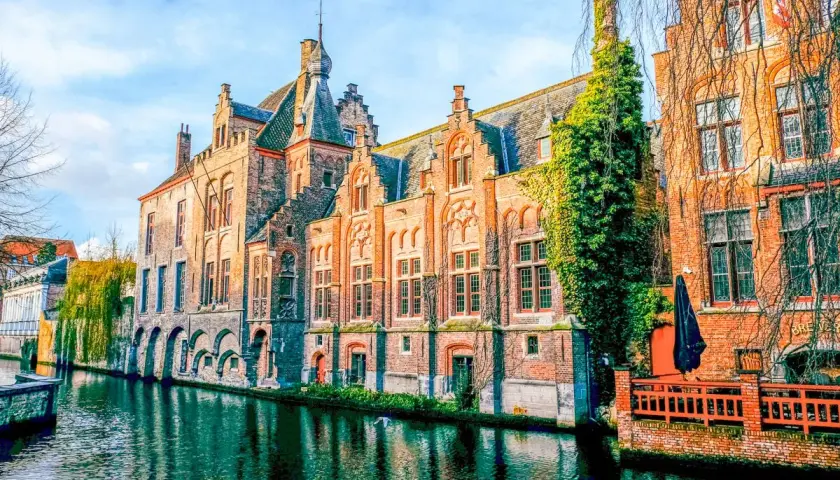Edificios históricos de ladrillo a lo largo de un canal, reflejando la belleza de Brujas, un viaje inolvidable de Bruselas a Brujas.