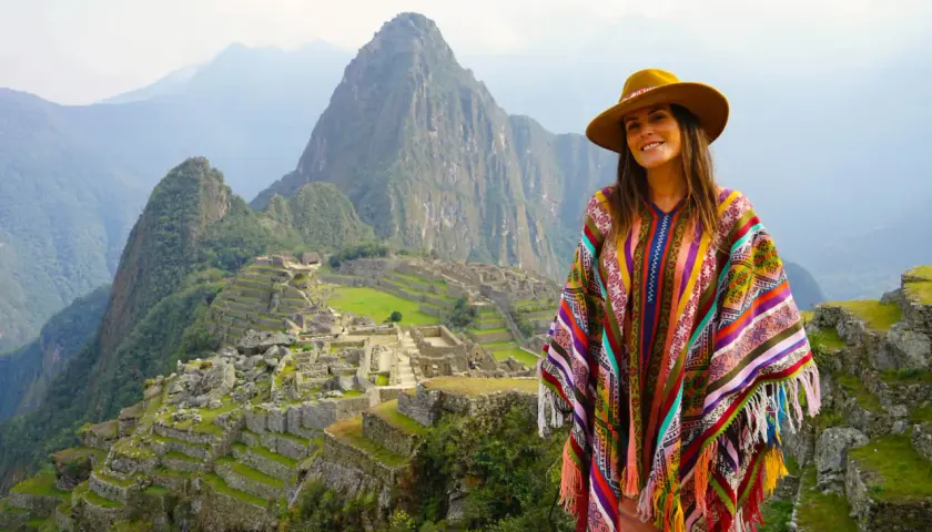Mujer con poncho colorido y sombrero en Machu Picchu, una experiencia inolvidable al viajar a Perú.