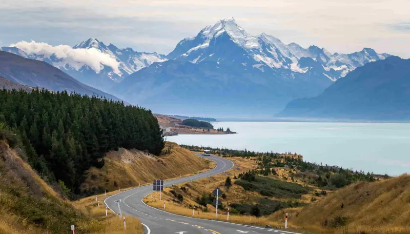 Carretera serpenteante hacia montañas nevadas y un lago turquesa. Impresionantes vistas de Nueva Zelanda que ver.