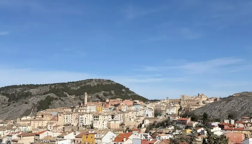 Vista panorámica de Cuenca, con sus casas de colores y tejados anaranjados, asentadas en una ladera rocosa bajo un cielo azul. Ideal para saber qué ver en Cuenca en un día.