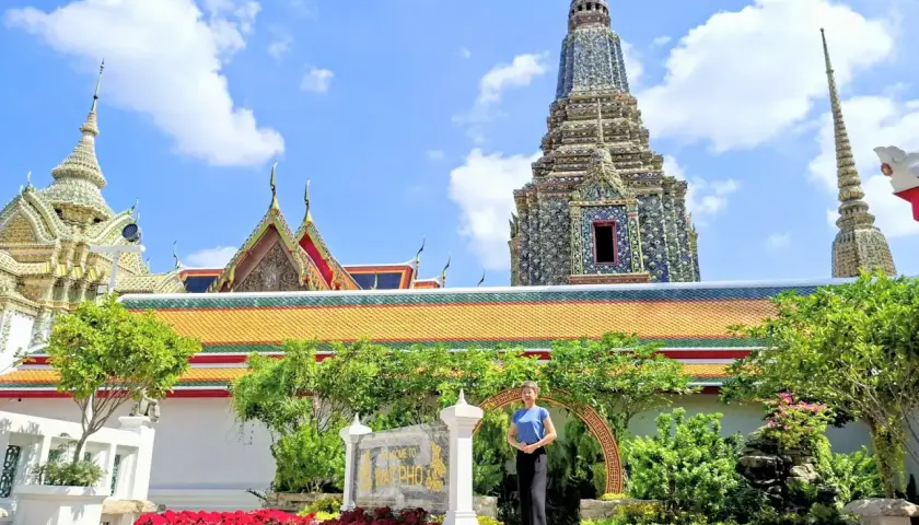 Disfrutando de un free tour en Bangkok, una mujer posa frente a templos tailandeses y pagodas ornamentadas bajo un cielo azul.