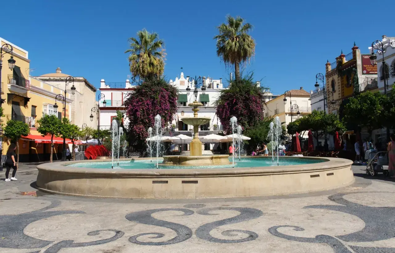 Fuente en plaza con palmeras y edificios blancos, ideal para saber qué ver en Sanlúcar de Barrameda.