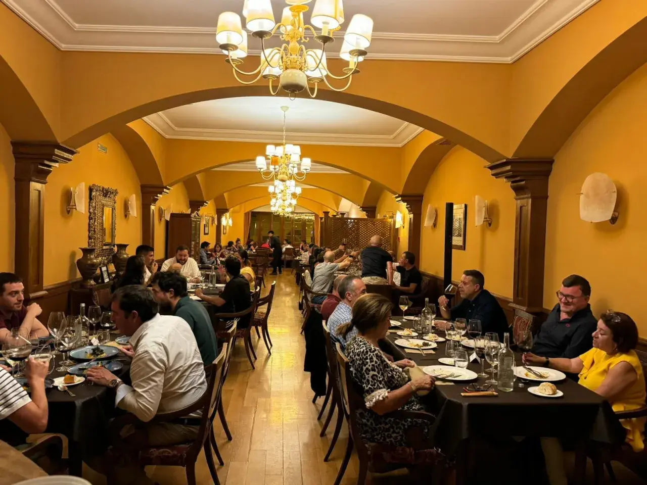 Gente disfrutando de una cena en un elegante salón con arcos y lámparas doradas. Un ambiente perfecto para comer en Olite.