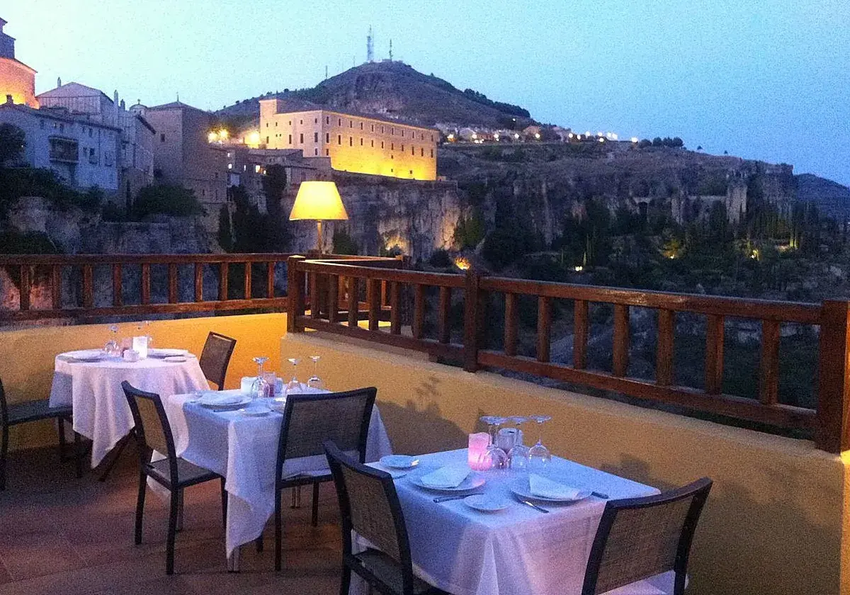Mesas puestas en terraza con vistas a la ciudad iluminada. Un lugar ideal donde comer en Cuenca al anochecer.