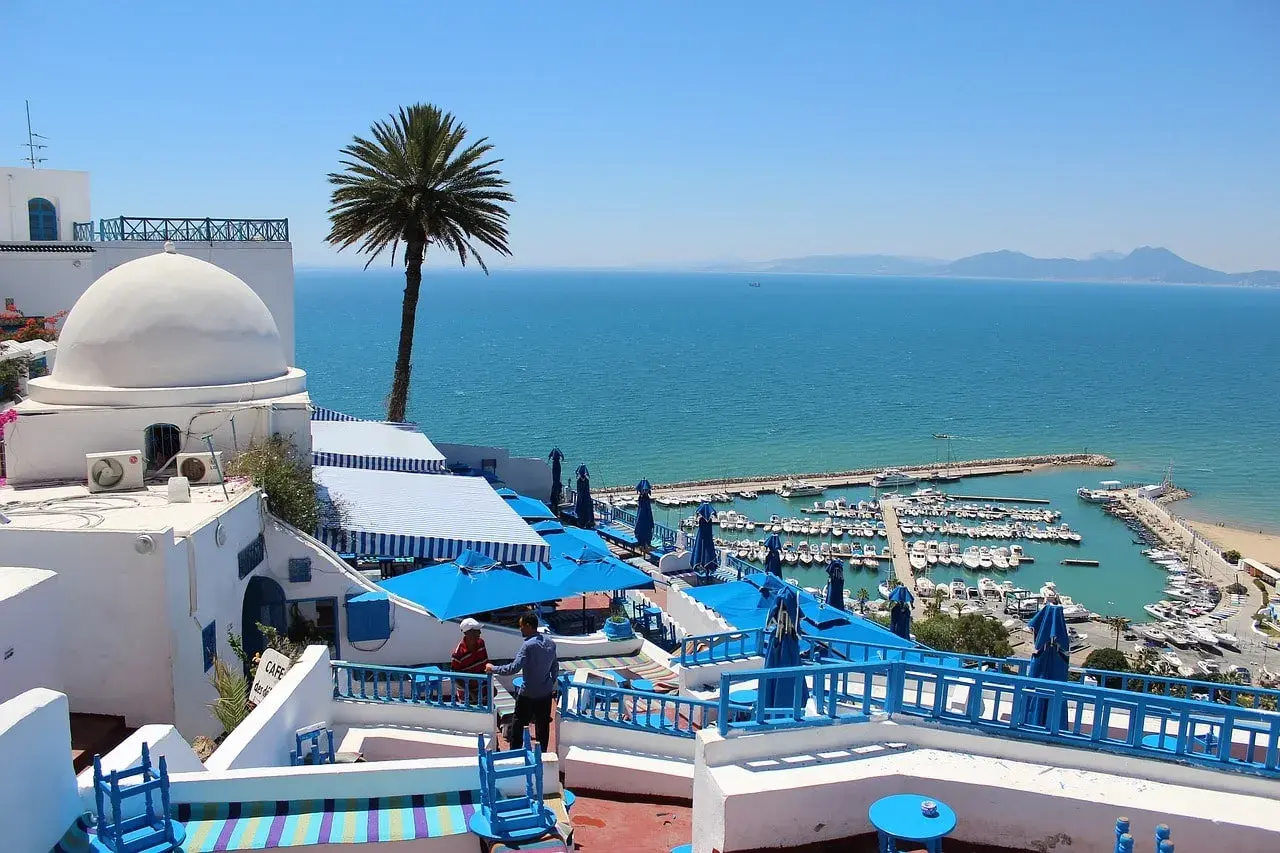 Vista de un puerto deportivo y el mar azul desde un café con cúpulas blancas y sombrillas azules. ¡Un sueño para viajar a Túnez!