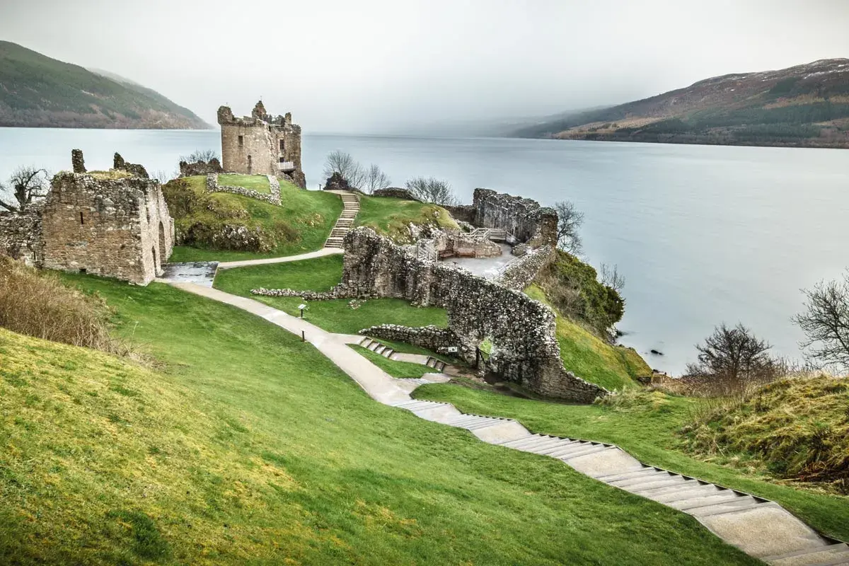 Ruinas de un castillo en una colina verde junto a un lago, ideal para un viaje a Escocia 7 días.