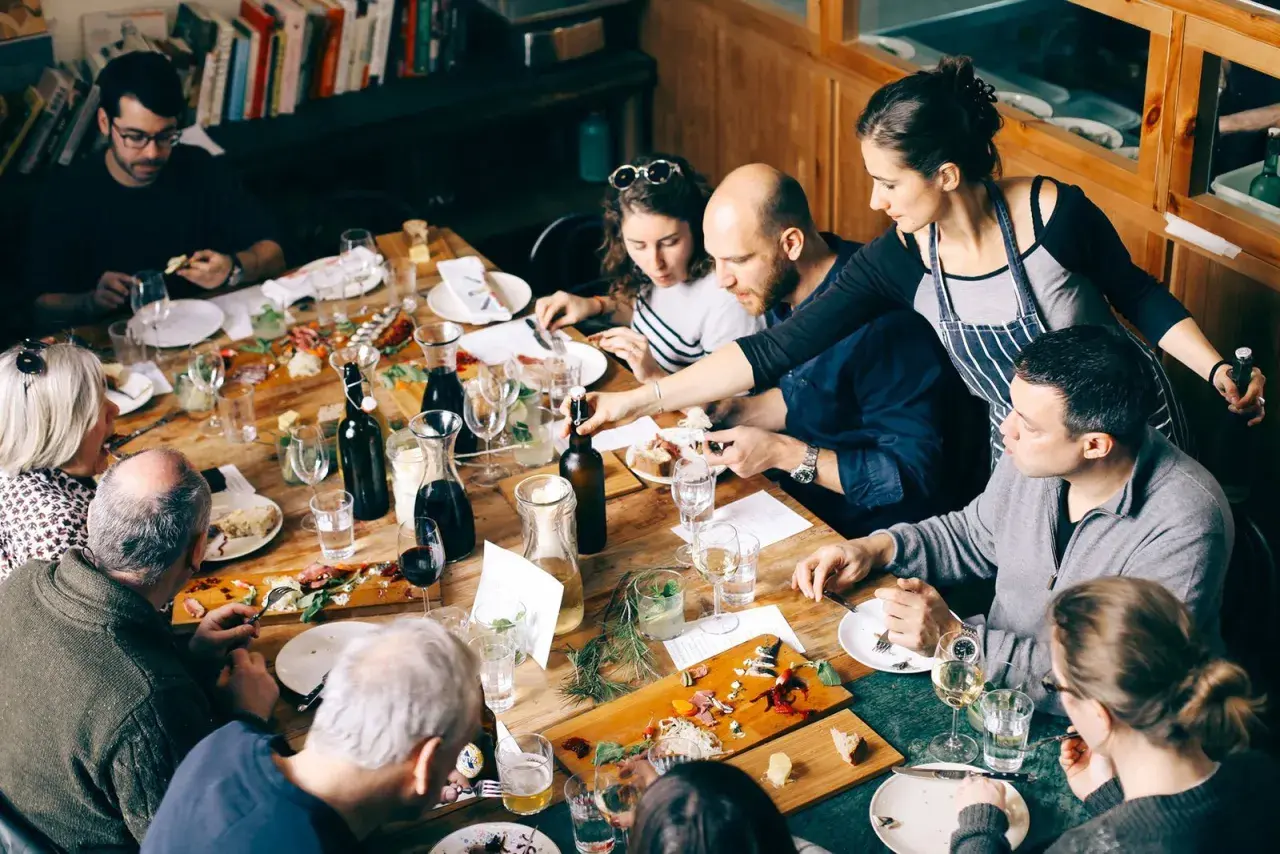 Gente disfrutando de una comida compartida en Barcelona. Una mesa llena de platos, botellas y copas.