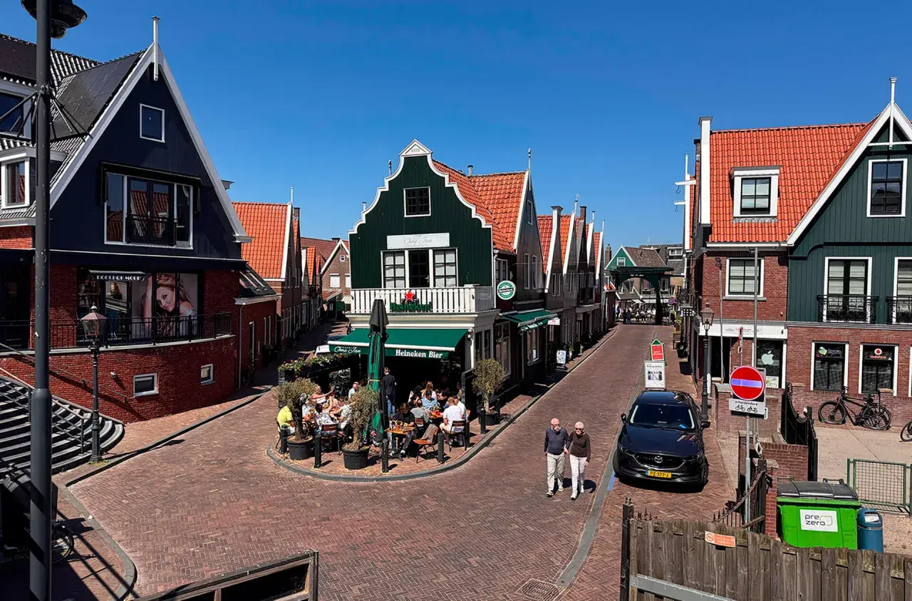 Un paseo por un pueblo holandés con casas de tejados rojos y fachadas coloridas. Un lugar ideal que ver en Holanda, con gente disfrutando en una terraza.