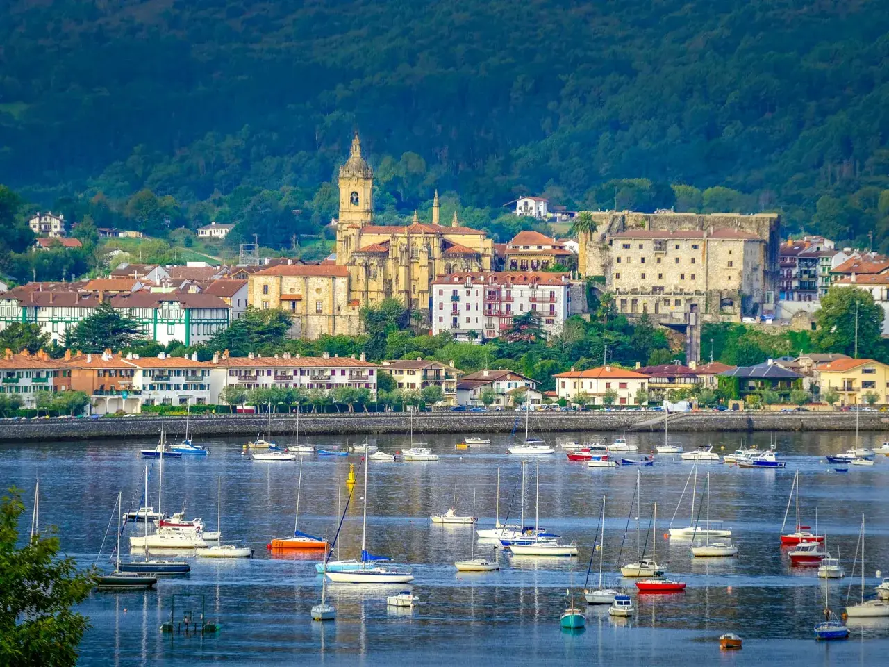 Vista de Hondarribia que ver: un puerto con veleros y barcos, y al fondo la iglesia y edificios históricos.