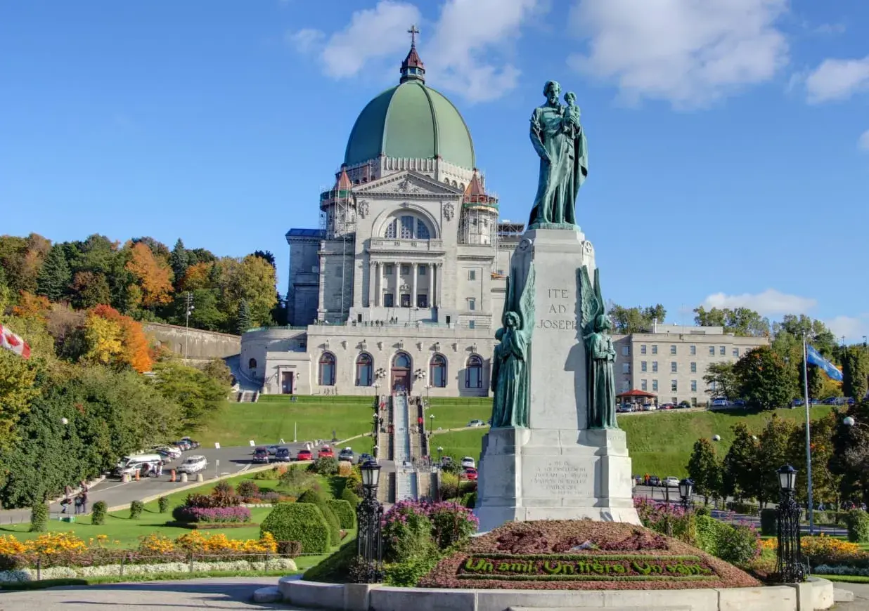 Estátua de São José frente a uma basílica imponente, ideal para visitas guiadas Montreal. Outono com árvores coloridas.
