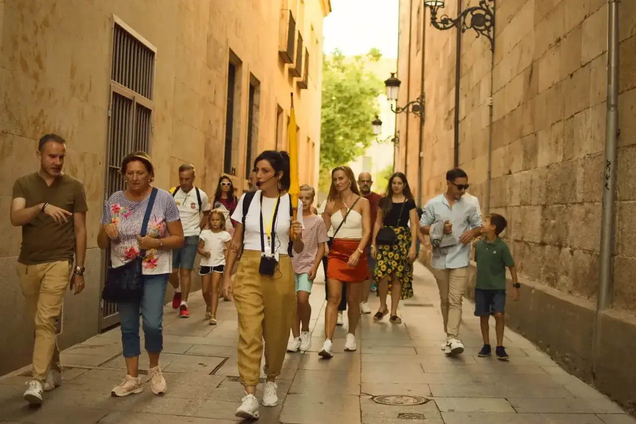 Un grupo disfruta de un free tour en Salamanca, guiado por una mujer con un micrófono, mientras pasean por una calle estrecha y empedrada.