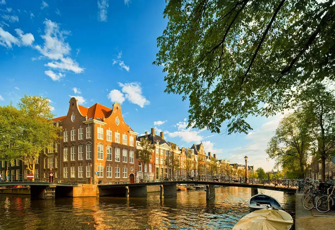 Un día perfecto para viajar a Ámsterdam: casas históricas junto a un canal, puentes y barcas bajo un cielo azul.