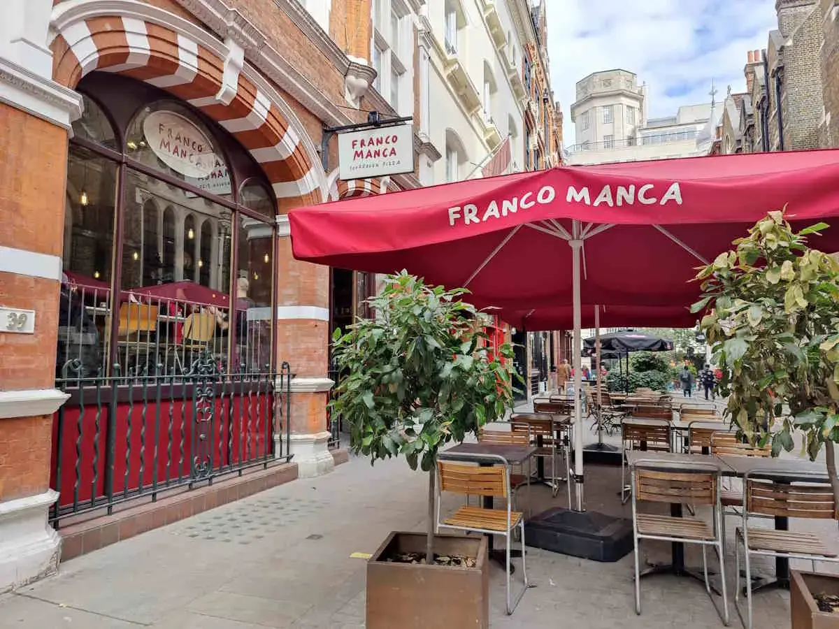 Franco Manca, un lugar ideal donde comer en Londres, con mesas al aire libre bajo sombrillas rojas.