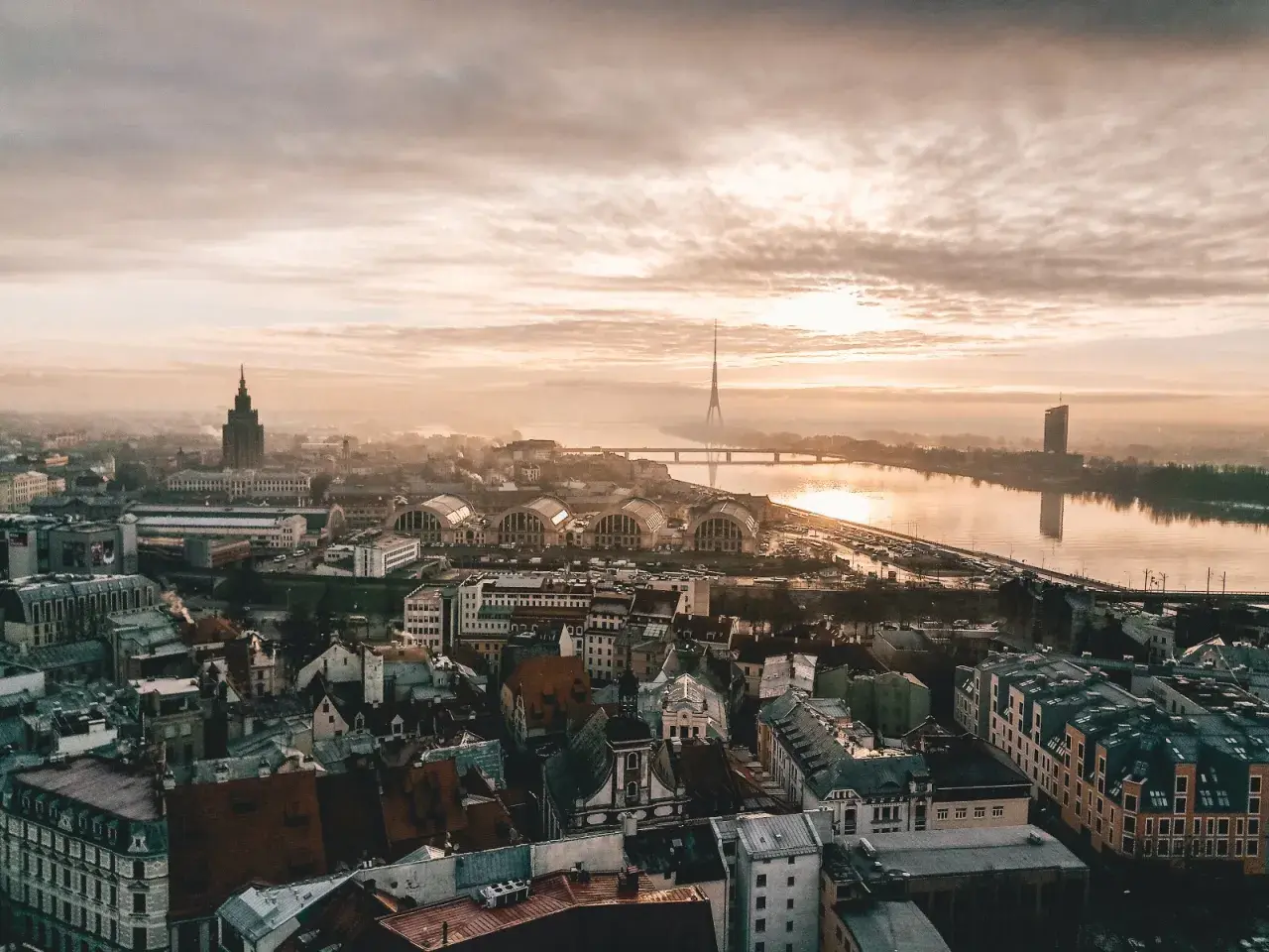 Vista aérea de Riga al amanecer, perfecta para planear tu viajar a Letonia. El río Daugava refleja el cielo nublado y la torre de televisión.