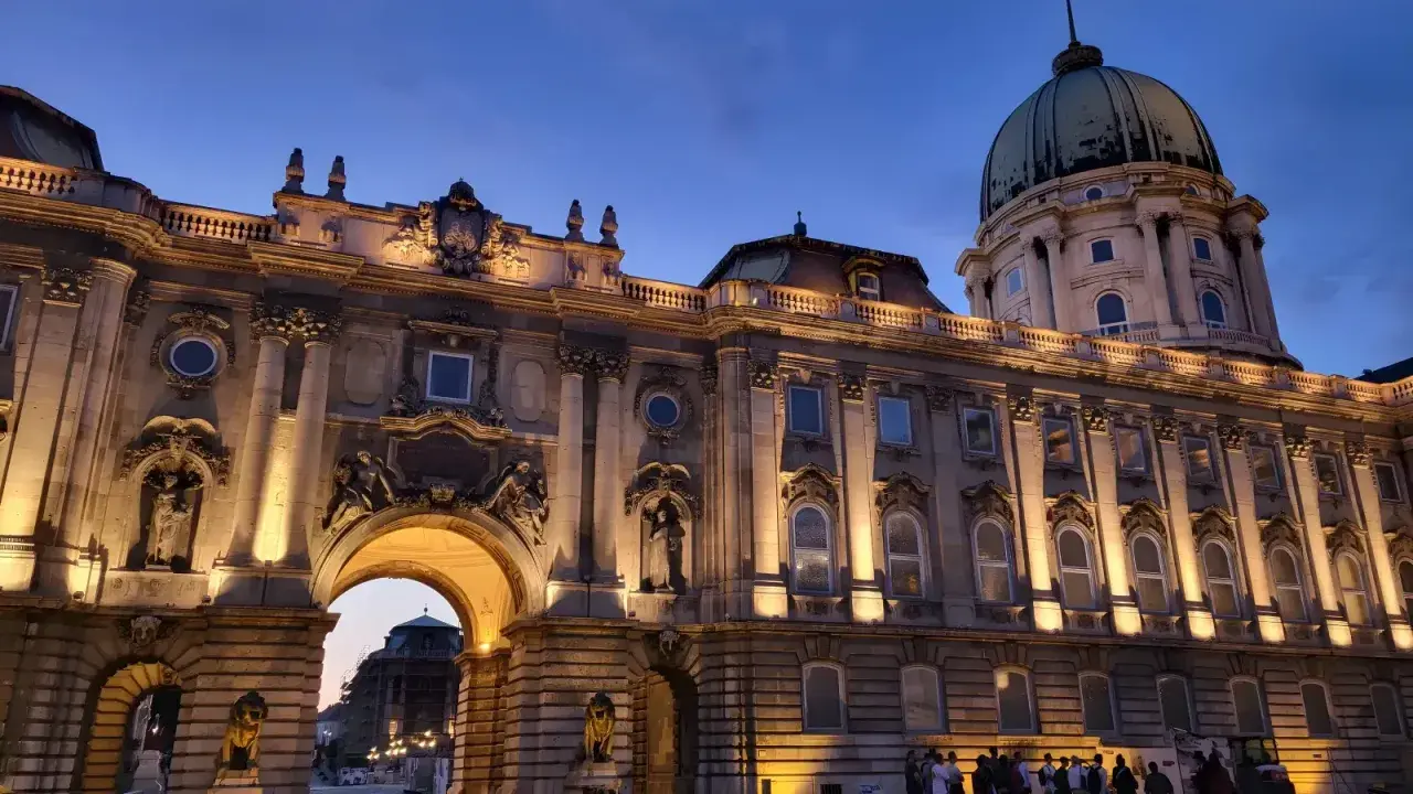 Palacio de Buda iluminado al atardecer, ideal para **free tours Budapest**. Una joya arquitectónica con cúpula verde y detalles ornamentados.