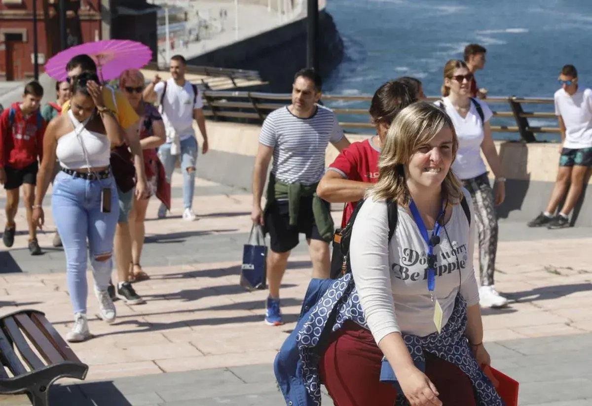 Un grupo de turistas participa en un free tour Gijón, disfrutando del paseo marítimo bajo un sol radiante.