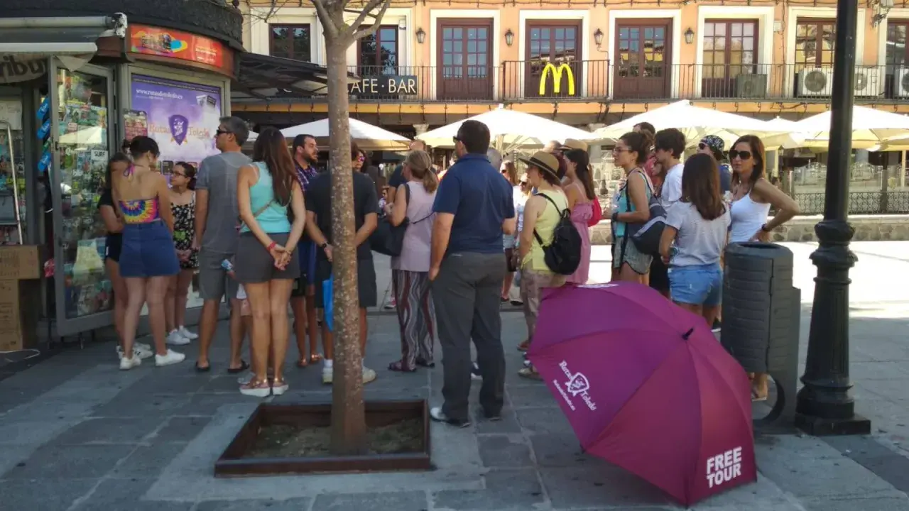 Grupo de turistas esperando un free tour a Toledo. Un paraguas morado con el logo de "Free Tour Toledo" está en primer plano.