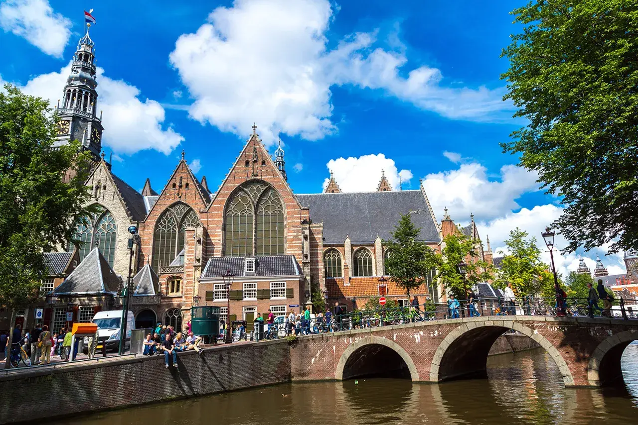 Gente disfrutando de un free tour en Ámsterdam, cruzando un puente sobre un canal frente a una iglesia histórica.