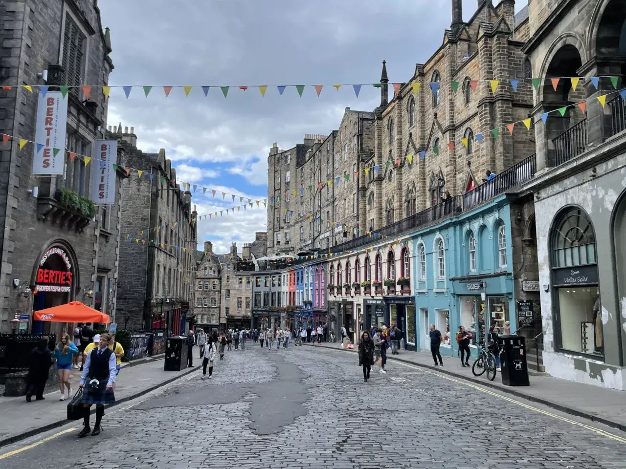 Calle adoquinada de Edimburgo, con edificios históricos y coloridas fachadas. Gente paseando, ideal para un **free tour Edimburgo**.